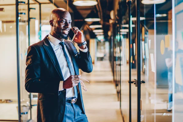 Positive dark skinned executive director dressed in formal wear discussing working plan of business company on smartphone device.Successful entrepreneur laughing during phone conversation on cellular