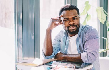 Uzaktan çekim sırasında tabletle masada oturup kameraya bakarken kendine güveni tam, sakin bir serbest çalışan.