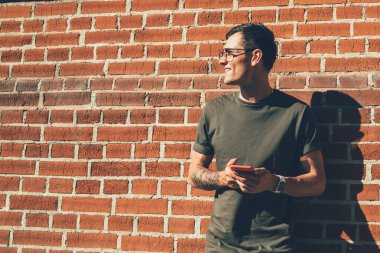 Elinde cep telefonu olan modaya uygun giyinmiş, elinde cep telefonu olan, şehrin duvarına bakarken gülümseyen, dijital aletli bin yıllık bir adam boş zamanlarında eğleniyor.