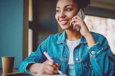 Mutlu siyahi kız öğrenci otokopi için eğleniyor ve sınava hazırlanırken akıllı telefon uygulamasını kullanarak arkadaşını arıyor, başarılı hipster kız cep telefonuyla konuşuyor.