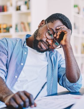 Çağdaş ofisin bulanık arka planı üzerinde çalışırken elinde gözlüklerle uyuyan yorgun siyah adam.