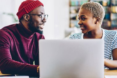 Gülümseyen Afro-Amerikan evlilikleri dizüstü bilgisayarla sohbet ederken, koyu tenli olumlu meslektaşlar ortak proje öğrenme fikirlerini tartışıyorlar.