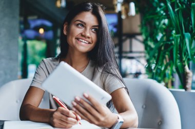 Kafeteryadaki uzak iş için dijital tablet ve wifi kullanan neşeli, güzel kadın blogcu, taşınabilir bilgisayar taşıyan not defterinde iş planlama bilgisi olan başarılı kadın.