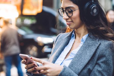 Ofisteki neşeli genç kadın, kulaklık ve cep telefonuyla müzik dinlemekten zevk alıyor.