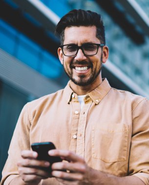 Görüş düzeltmesi için gözlüklü mutlu duygusal bir adamın yarım boy portresi kameraya bakıyor ve modern teknoloji, iletişim ve dijitalleşme kavramını kullandığı için zaman boyunca gülüyor.