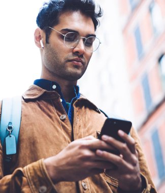 Alttan bakınca, kulaklıklı, kahverengi süet ceketli, akıllı telefondan yazan ve New York caddesinde dururken müzik dinleyen düşünceli, yakışıklı, tıraşsız bir erkek görüyorum.