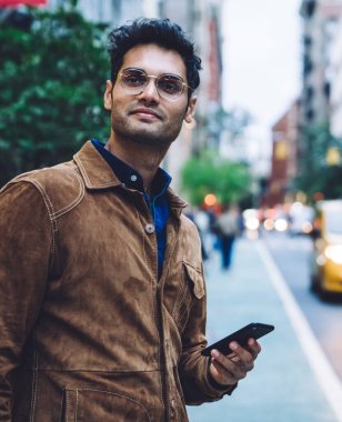 Yakışıklı, etnik esmer, ceketli, gözlüklü, akıllı gözlüklü, güpegündüz trafik şeridinin yanında duran yakışıklı bir adam.