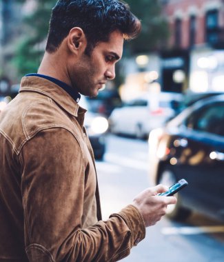 Gündelik giysiler içinde, modern dijital akıllı telefonu iletişim, internette gezinme ve mesajlaşma için kullanan yakışıklı bir erkeğin yan görüntüsü.