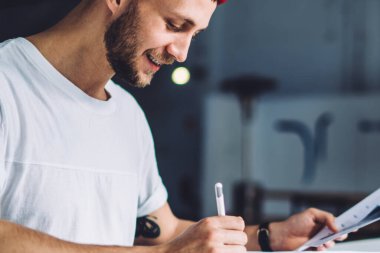 Kırmızı şapkalı genç adam, elinde akıllı telefon tableti defteriyle masada oturuyor ve iş sırasında gazetelere notlar yazıyor.