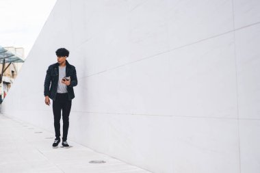 Gündüz vakti şehir caddesi tünelinde yürürken günlük kıyafet giyen modern stil, kendine güveni tam bir etnik adam tablet üzerinde geziniyor.