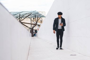 Gündüz vakti şehir caddesi tünelinde yürürken günlük kıyafet giyen modern stil, kendine güveni tam bir etnik adam tablet üzerinde geziniyor.