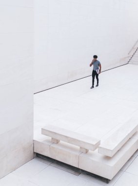 Beyaz iş merkezinde elinde belgelerle dolaşırken akıllı telefondan konuşan gündelik kıyafetlerle üst düzey etnik erkek.