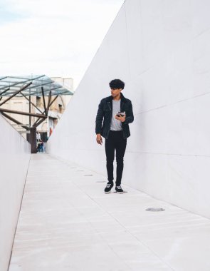 Gündüz vakti şehir caddesi tünelinde yürürken günlük kıyafet giyen modern stil, kendine güveni tam bir etnik adam tablet üzerinde geziniyor.