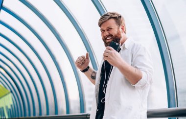 Olumlu erkek meloman, iyi haberlerle gelen sesli mesajdan mutlu müzik hobisi için boş zamanlarında dinleyen, günlük kıyafetli ve radyo eğlencesi sırasında evde dans eden kulaklıklı genç adam.