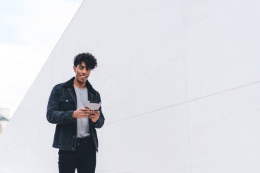 Modern stil gülümseyen pozitif esmer Afrikalı Afrikalı Amerikalı adam gün ışığında şehir caddesi tünelinde yürürken tablet üzerinde geziniyor.