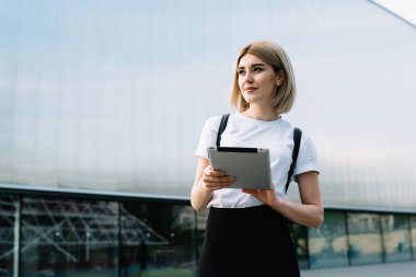 Günlük giysiler içinde gülümseyen genç bir kadın tableti karıştırıyor ve ofis binasının yanındaki caddede dikilirken hayal kurmaktan vazgeçiyor.