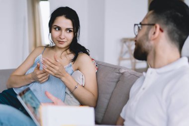 Modern, çok ırklı kadın ve erkek, gündelik giysiler içinde evlerinde oturmuş, kanepede oturup birbirlerine bakıyorlar.