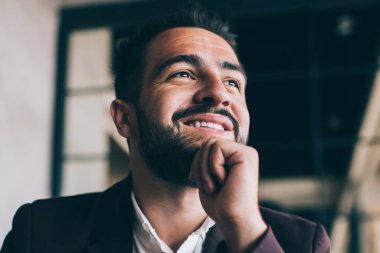 Heyecanlı, karizmatik, zarif takım elbiseli, elinde kalemle iş yerinde yüzünü çevirerek çenesine dokunan bir proje yaratan bir adamdan.