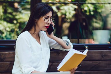 Klasik gözlüklü İspanyol serbest yazar, uluslararası cep telefonu konuşmaları sırasında proje detaylarını tartışmak için not defterinden bilgi kontrol ediyor, milenyum kadını hareketlilik bağlantısı kullanıyor