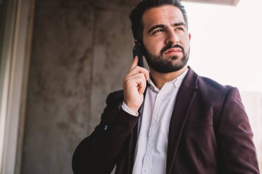 Düşünceli beyaz erkek, modaya uygun resmi ceketli, dışarıda hücresel sohbetler yaparak vakit geçiriyor, başarılı, kendinden emin iş adamı, akıllı telefondan iyi bağlantıları kullanarak başka yere bakıyor.