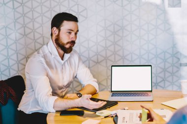 Resmi gömlekler giymiş, dizüstü bilgisayarlı masada oturan modern ciddi iş arkadaşları ofis alanındaki akıllı telefonu belgelerler.