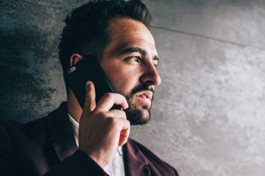 Zarif takım elbiseli ciddi bir genç, akıllı telefon kullanıyor. İş arkadaşıyla konuşuyor. Proje saatlerini iş yerinde geçirip gözlerini kaçırıyor.