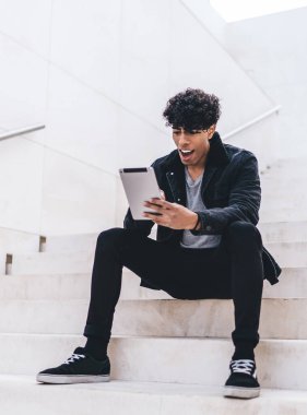 Günümüz modası geçmiş esmer, Afro-Amerikalı bir adam gündüz vakti şehir merdivenlerinde otururken tablet üzerinde geziniyor.