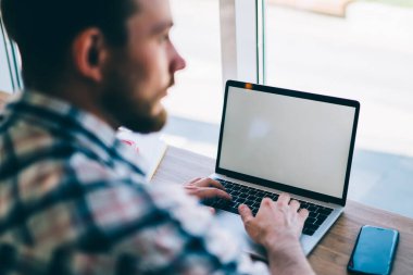 Yoğunlaşmış, koyu renk saçlı, günlük gömlekli, kahve dükkanındaki masada oturan dizüstü bilgisayarla yeni projenin planını yazan adam.