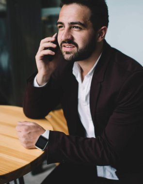 Resmi ceketli yakışıklı beyaz sakallı adam modern cihazlar ve 4G internet bağlantısı kullanarak cep telefonuyla konuşuyor. Milenyum işadamı akıllı telefon aramasından memnun.