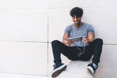 Elektronik kulaklıklı mutlu erkek blogcu sosyal ağlardan sanal takipçilerle çevrimiçi video konferansında dokunmatik ped üzerinde 4G kablosuz bağlantı kullanıyor, milenyum jenerasyon iletişimi kavramı