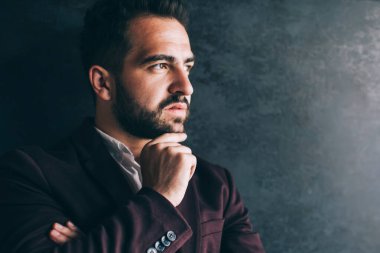 Düşüncelere dalmış zarif takım elbiseli, düşünceli, düşünceli bir etnik adamın çalışma alanında durup gözlerini kaçırması.