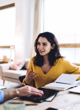 Neşeli ve iyimser bayan serbest çalışan açık dizüstü bilgisayar ve defterin önünde oturuyor ve müşteriyle konuşuyor.