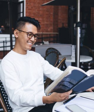 Entellektüel Asyalı neşeli, gözlüklü, ders kitabı okuyan, sokak yemekhanesinde edebiyat ödevi yapan modern bir adam.