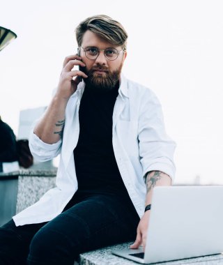 Önemli uluslararası akıllı telefon konuşmaları, dolaşım iletişimi ve uzaktan çalışma kavramları yaparken kameraya bakan, optik gözlüklü, ciddi bir erkek programcının portresi