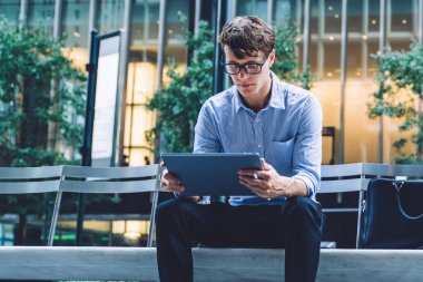 Gözlüklü yakışıklı genç bir adam. Ofis binasının önündeki bankta oturuyor. Manhattan, New York 'ta bir sokakta tablet kullanıyor.