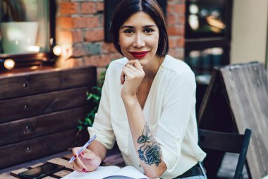 Şehir kafeteryasının dışında otururken yeni bir makale yazmak için ilham veren çekici kadın blogcu, terasta oturan küçük bayan sahibi.