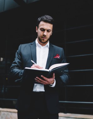 Modern şehir caddesinde dururken resmi takım elbiseli bir yöneticinin randevu defterine notlar yazmasından.