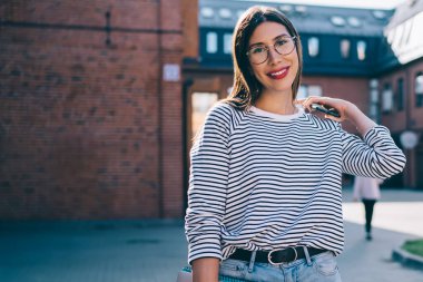 Üniversite kampüsünde modern dizüstü bilgisayarı olan mutlu kız öğrencinin yarım boy portresi, kameraya gülümseyen gözler için optik gözlüklü pozitif hipster kız.