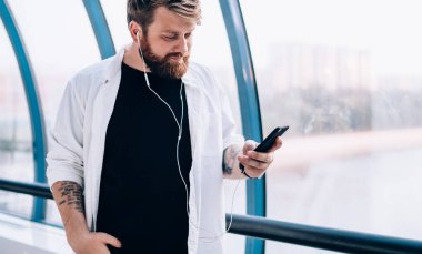 30 'lu yaşlardaki adam, elektronik kulaklıklardan çalma listesi kullanarak içeride durup müzik dinlerken iş arkadaşından gelen e-postayı kontrol ederken, hipster adam mesajları aldı ve oyuncu şarkısını seçti.