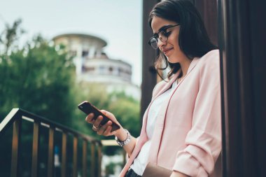 Kağıt klasörü ve günlüğü olan meşgul bir kadının cep telefonundan mesajları kontrol etmesi ve binanın yanında dururken gülümsemesi.