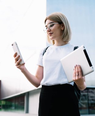 Gözlüklü, sıradan kıyafetler giyen, gülümseyen ve akıllı telefonu dikkatle kullanan bir kadının ofis binasının yanındaki caddede durmasına sevindim.