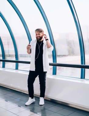 Beyaz tişörtlü karizmatik gülen adam kollarını sıvadı ve beyaz spor ayakkabılar, yaya köprüsünde kulaklıkları ayarlayan müzik dinlemek için cep telefonu kullanıyor.