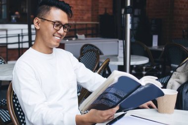 Entellektüel Asyalı neşeli, gözlüklü, ders kitabı okuyan, sokak yemekhanesinde edebiyat ödevi yapan modern bir adam.