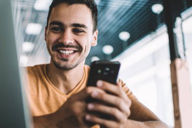 İş yerindeki masada oturan, arkadaşlarıyla cep telefonu sohbeti yapan, günlük kıyafetli, pozitif bir adamdan.