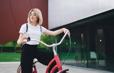 Gözlüklü, kendine güveni olan, kırmızı bisikletli ve sosyal medyada gezinen akıllı telefonlu, gözünü çevirmiş bir kadın.