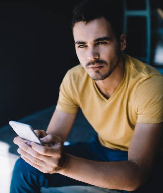 Ciddi bir şekilde endişeli genç bir erkek elinde akıllı bir telefonla zor bir kararı düşünürken dalgın dalgın bakıyor.