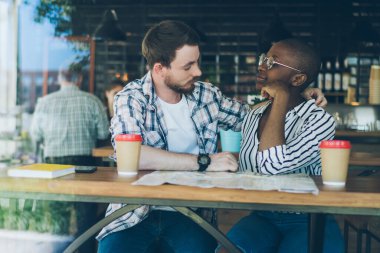 Kot pantolonlu çok ırklı bir çift şehrin karşısındaki kafede kahve içiyorlar.