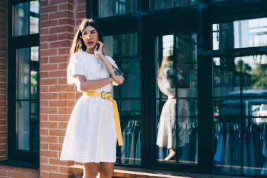 Şık sarı güneş gözlüklü düşünceli bayan öğrenci, başka tarafa bakıyor ve bilgiyi düşünüyor, modaya uygun giyinmiş İspanyol hippi kız şehir ortamında şık bir aksesuar takıyor.