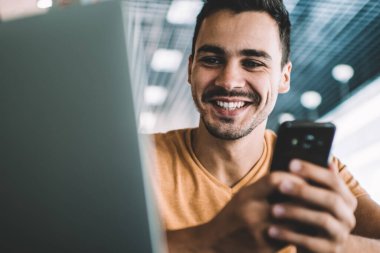 İş yerindeki masada oturan, arkadaşlarıyla cep telefonu sohbeti yapan, günlük kıyafetli, pozitif bir adamdan.