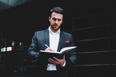 Modern şehir caddesinde dururken resmi takım elbiseli bir yöneticinin randevu defterine notlar yazmasından.